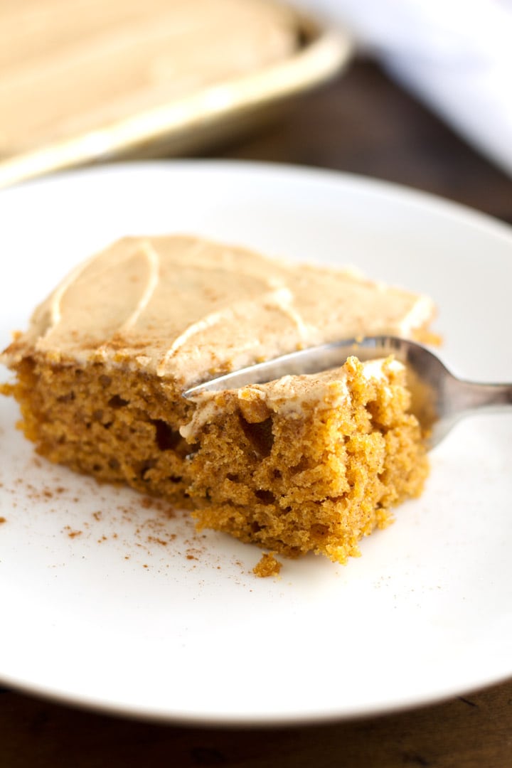 Piece of pumpkin sheet cake on plate with whole cake in background.