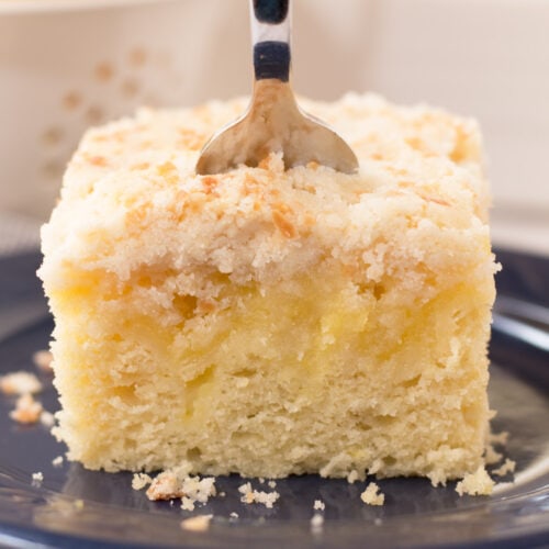 Lemon coffee cake with layer of lemon curd and crumb topping on a blue plate with fork in the middle.