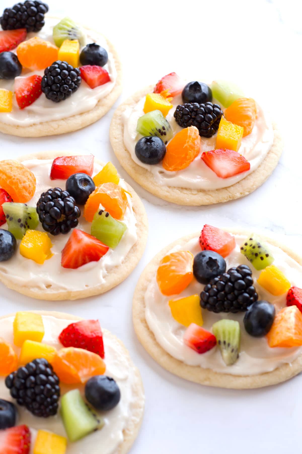 Five fruit pizzas cookies lined up on the counter.