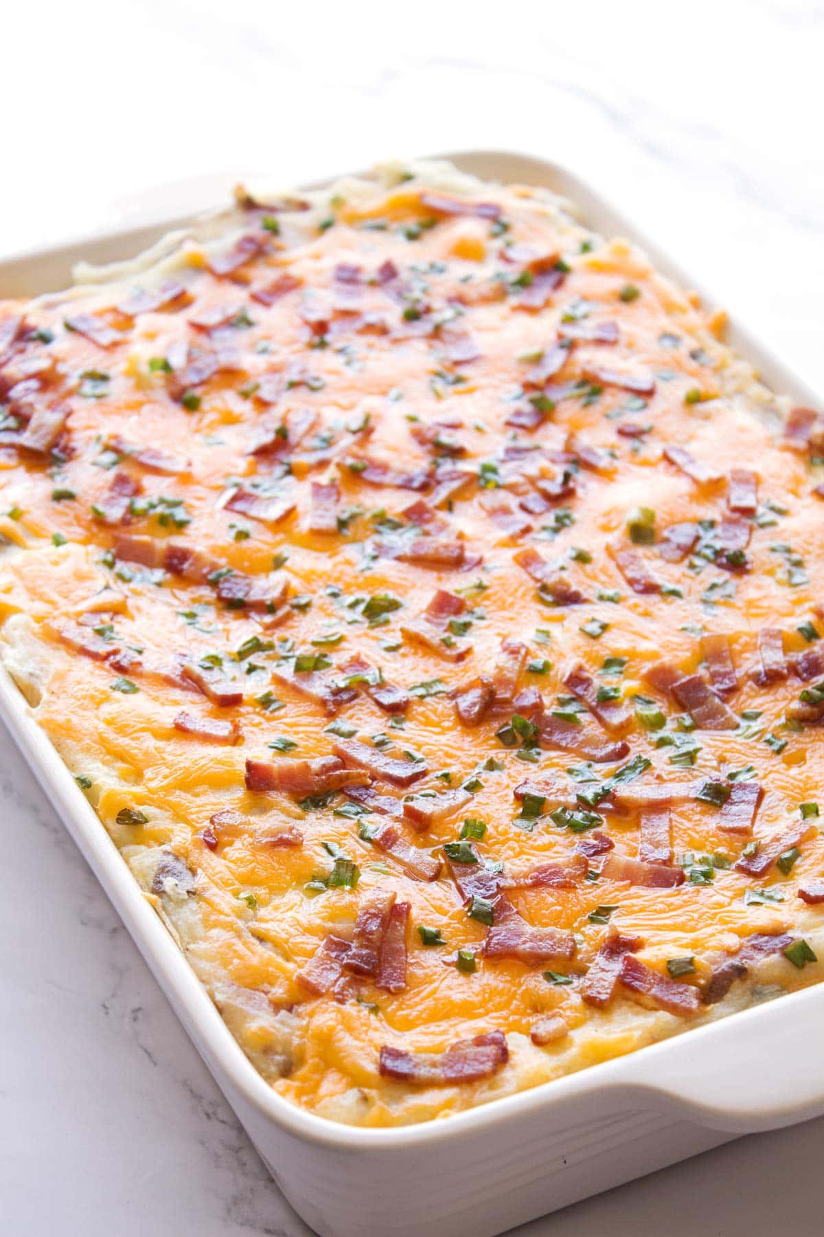 White baking dish with loaded baked potato bake with sour cream.