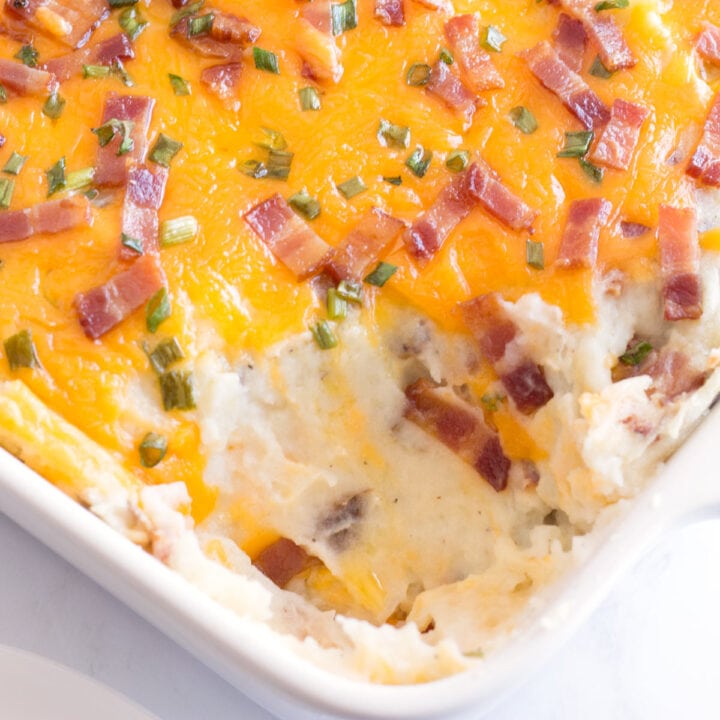 Loaded baked potato casserole in white baking dish with a scoop removed from the front.