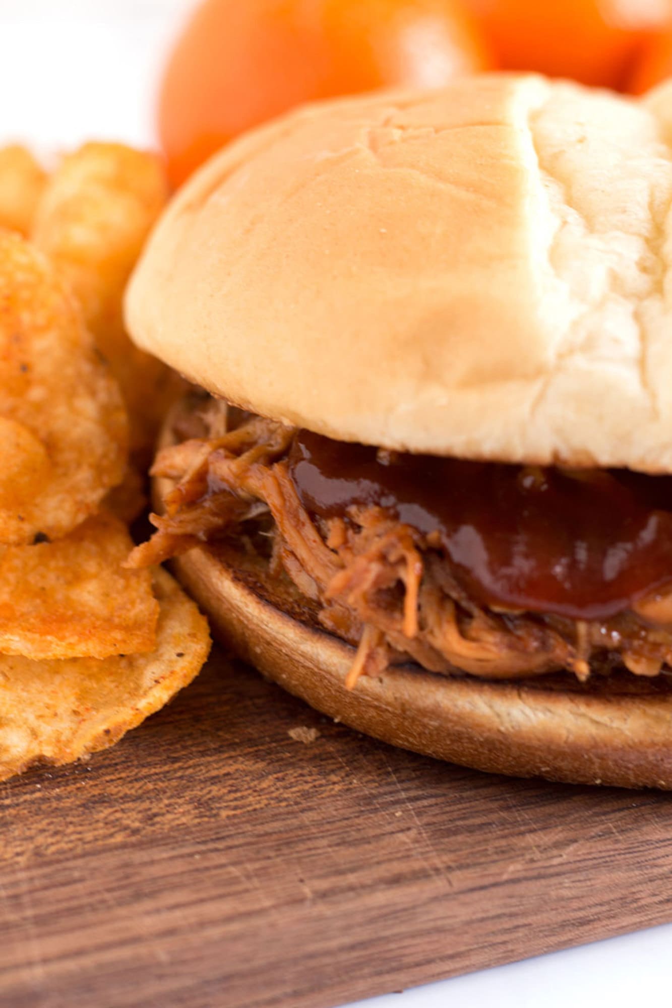 Shredded BBQ chicken on a bun with chips and tangerines.