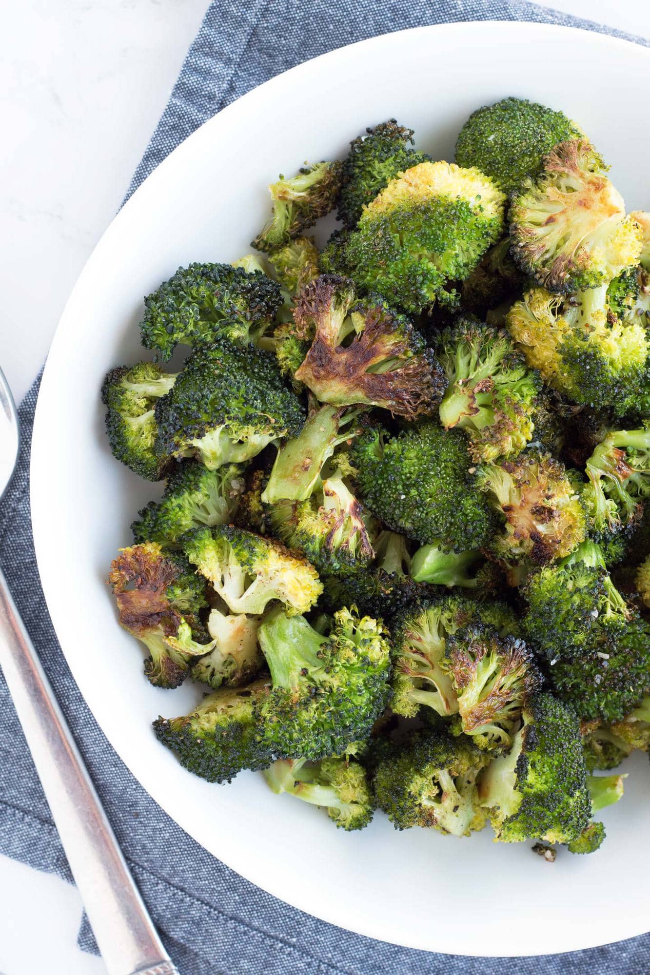 White bowl of perfect oven roasted broccoli with grey towel