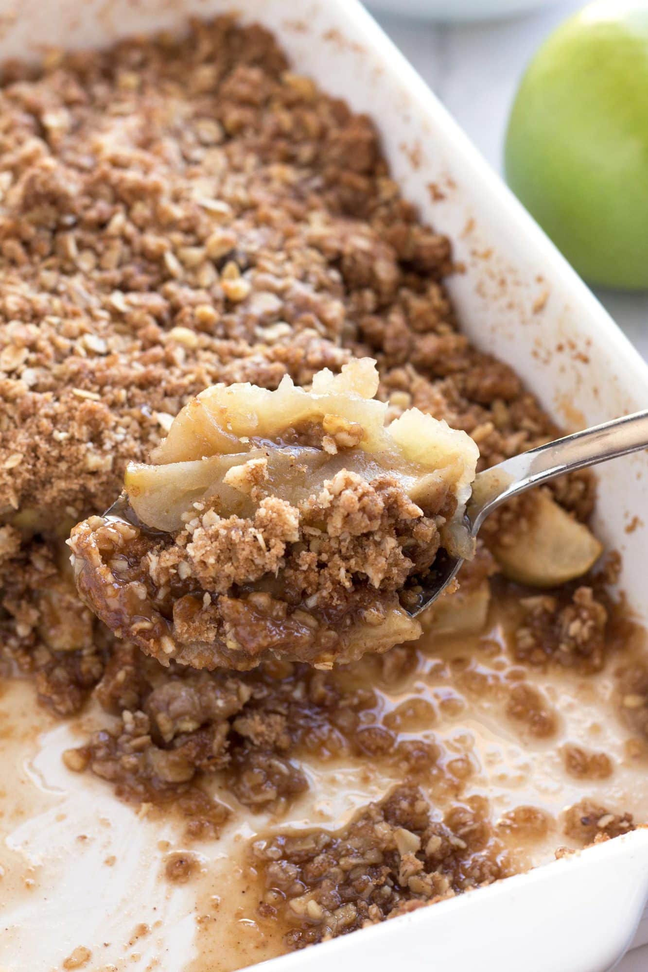 Spoon with scoop of easy apple crisp recipe coming out of baking pan