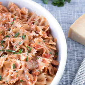 Chicken Piccata Pasta in white bowl with parmesan cheese and grater on counter