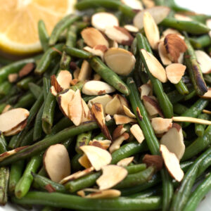 Green beans almondine with almonds and a lemon on a platter