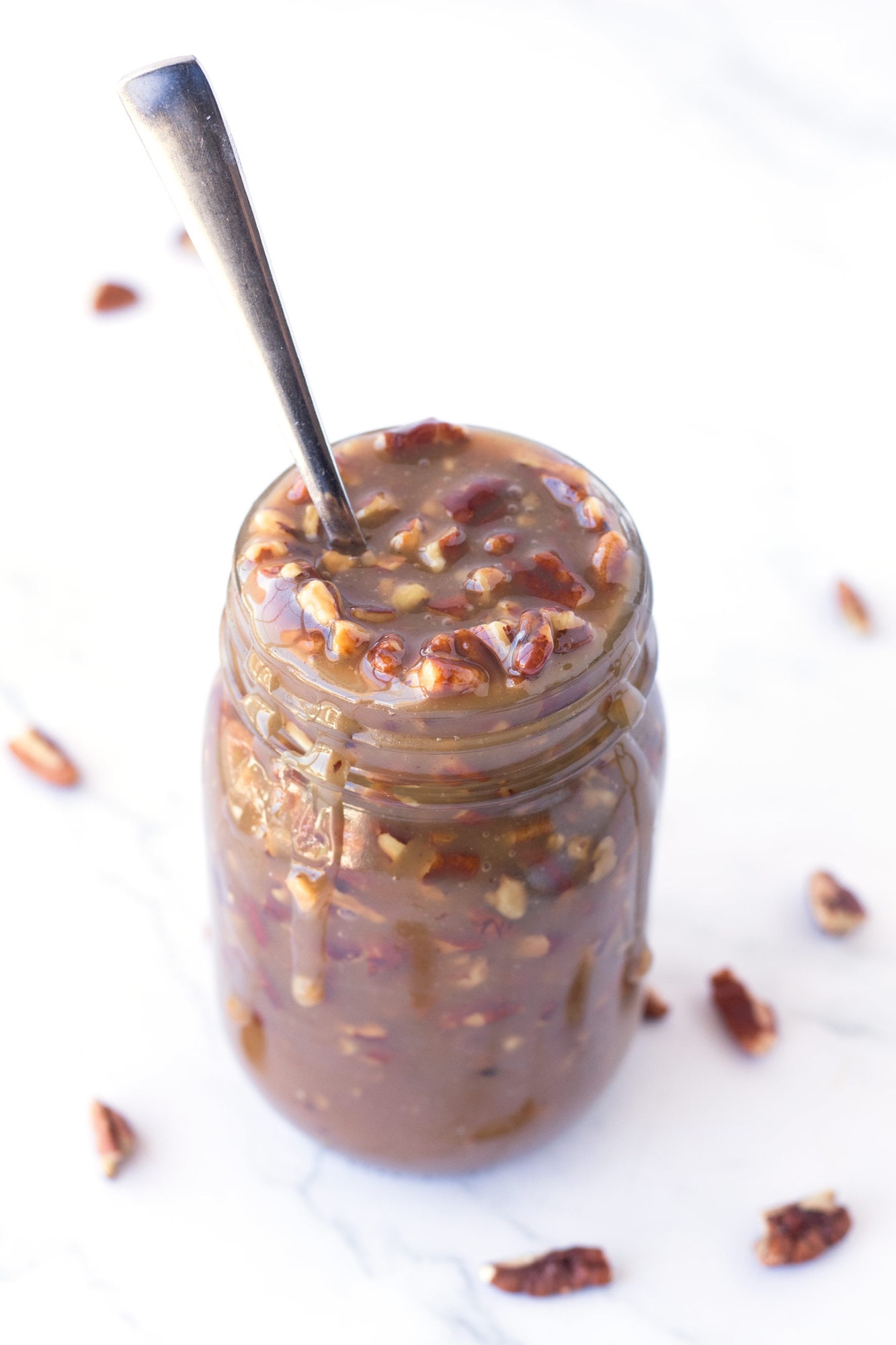Jar of microwave caramel pecan sauce with a spoon inside.