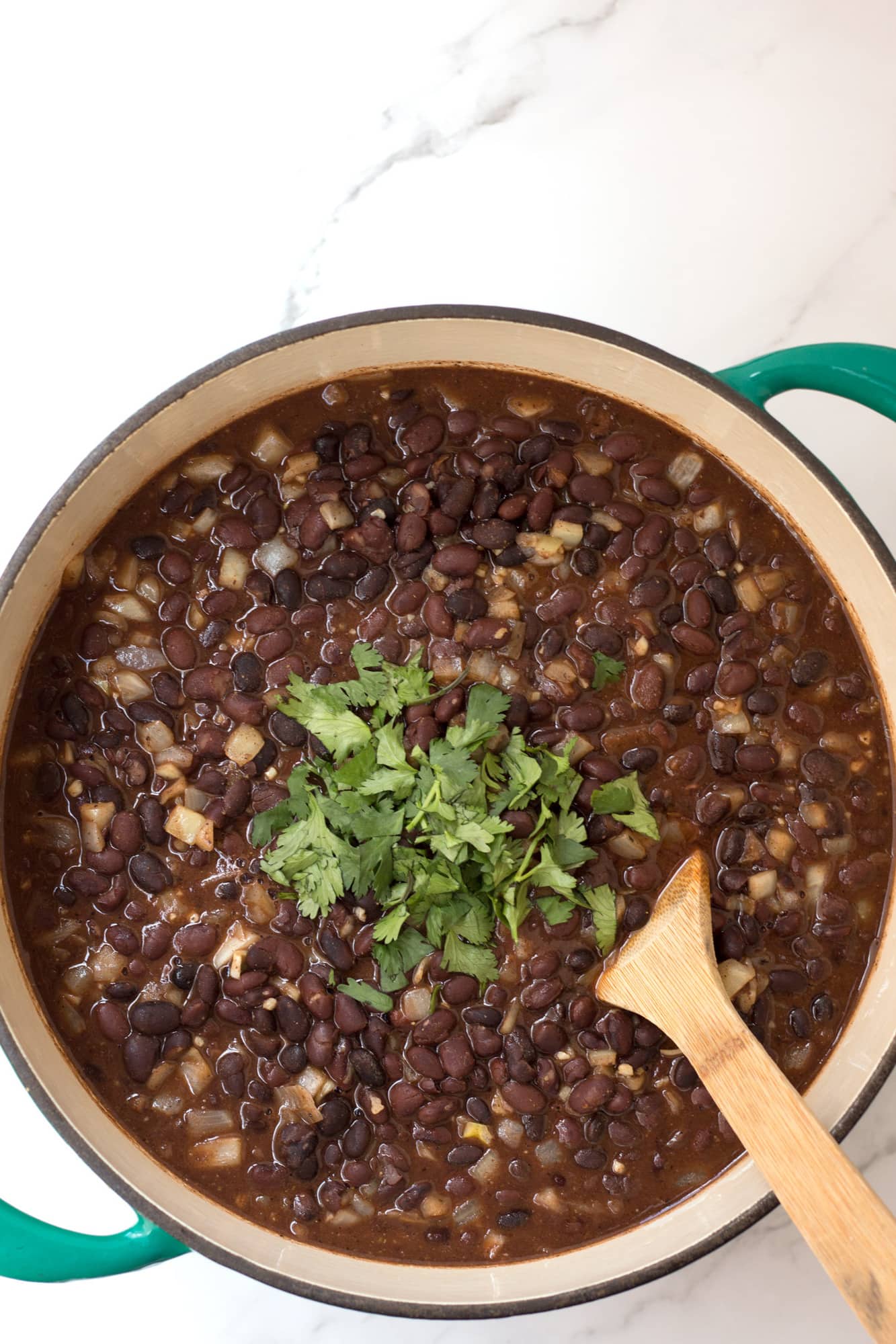 Black beans with a wooden spoon in a dutch oven.
