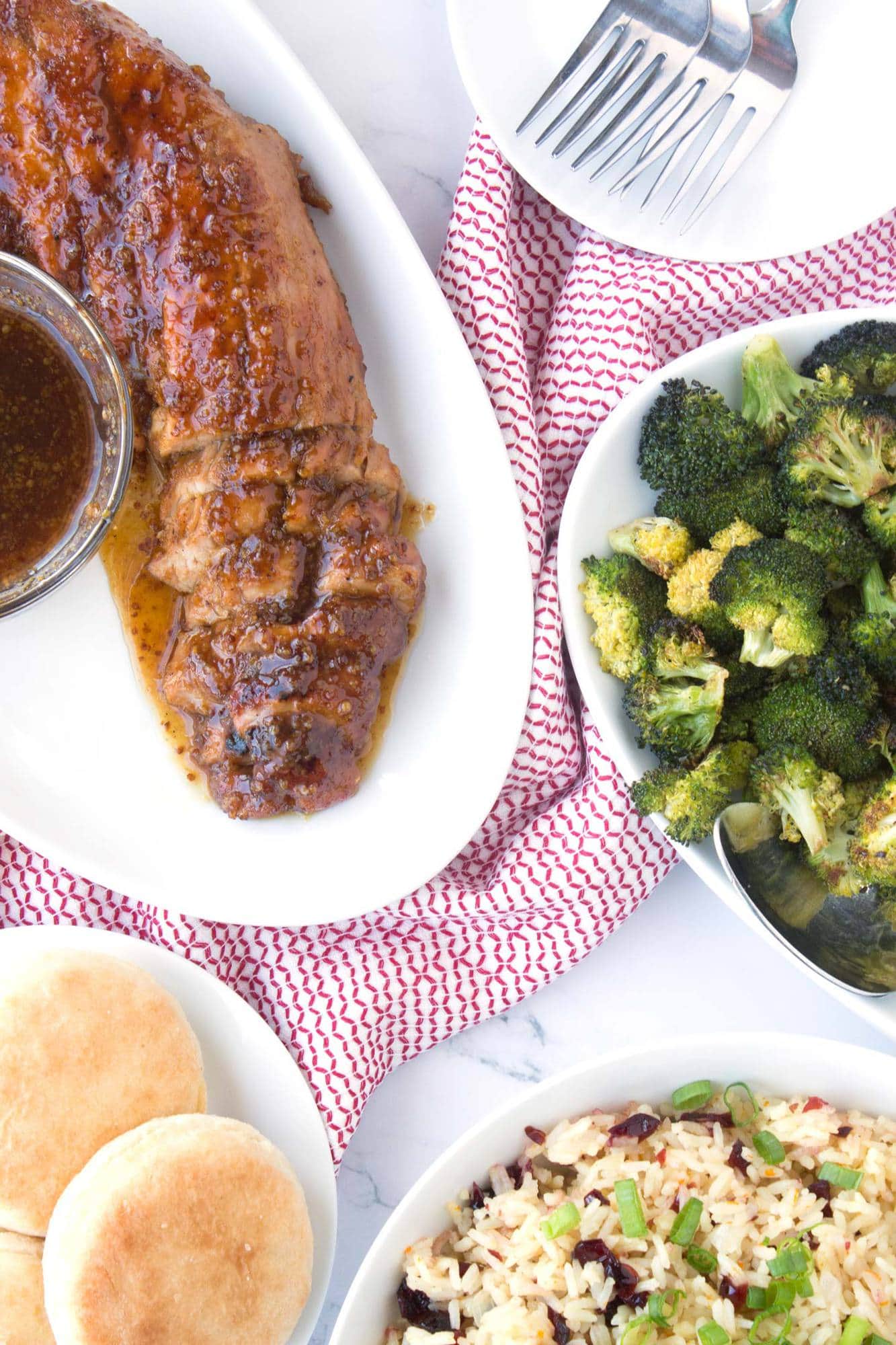 Pork Tenderloin with orange cranberry rice, broccoli, and biscuits on serving platters for Sunday Dinner.