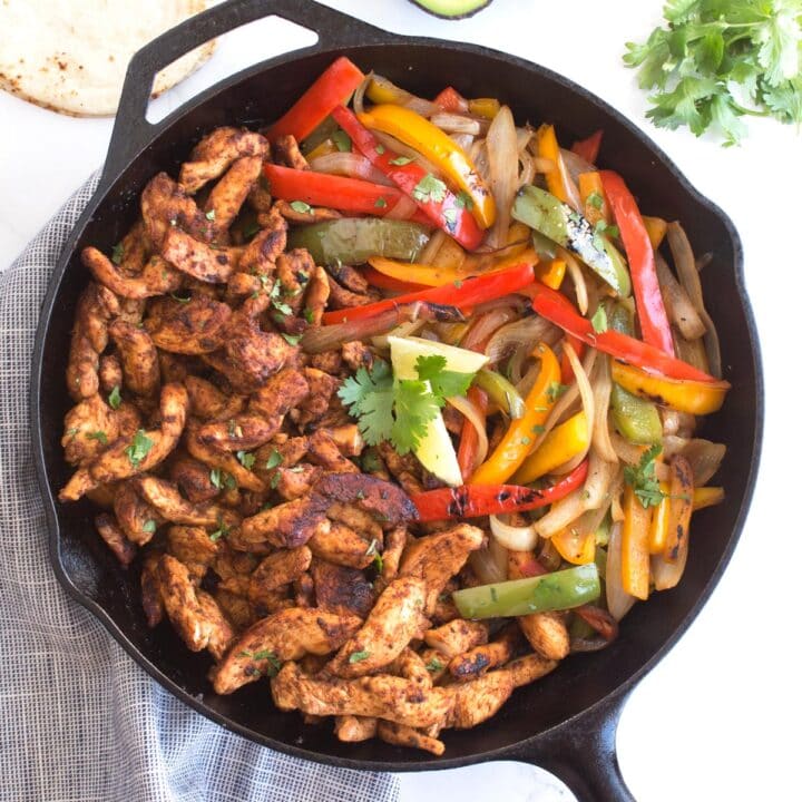 Overhead of cast iron skillet with chicken fajitas and blue towel.