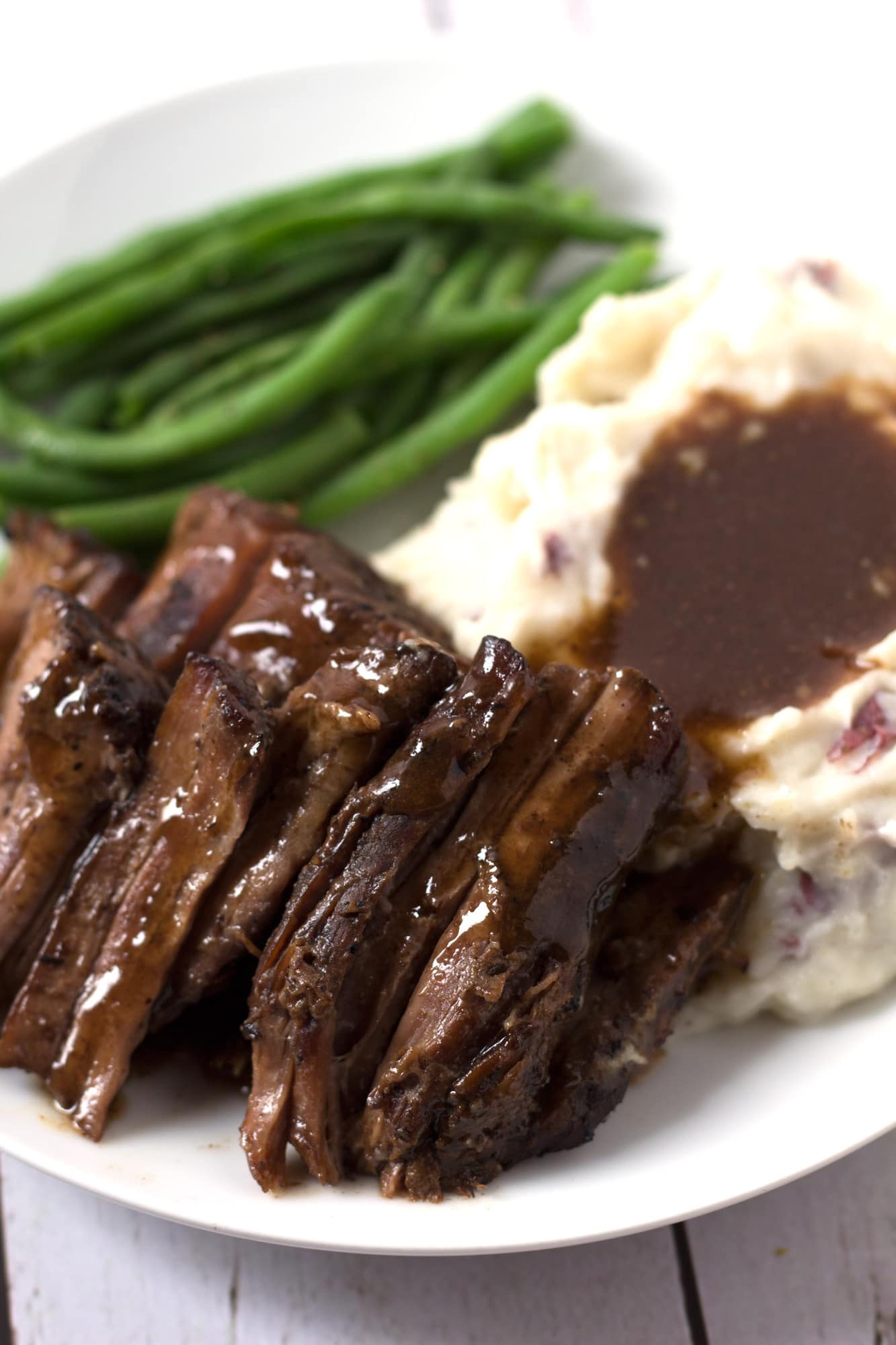 Pot roast, mashed potatoes, and green beans on a plate.