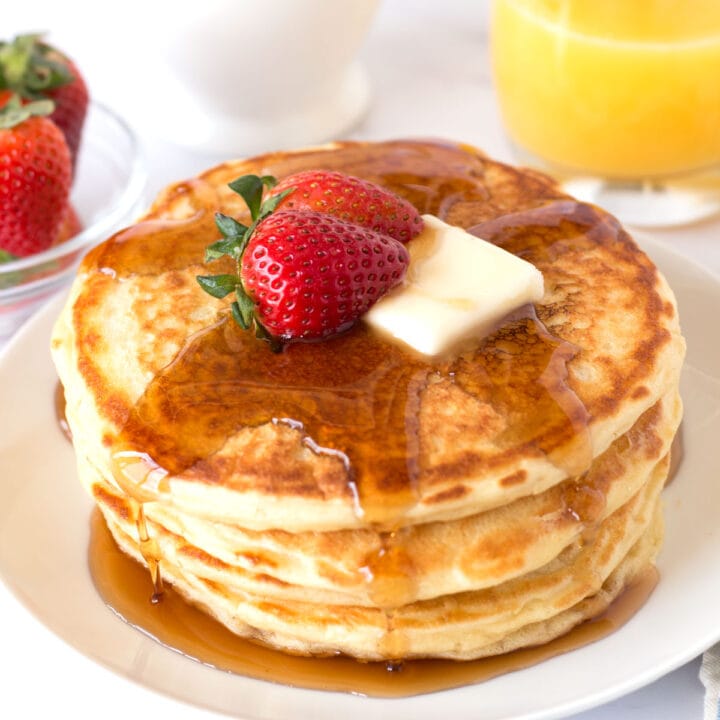 Panckaes on a white plate with strawberries and syrup.