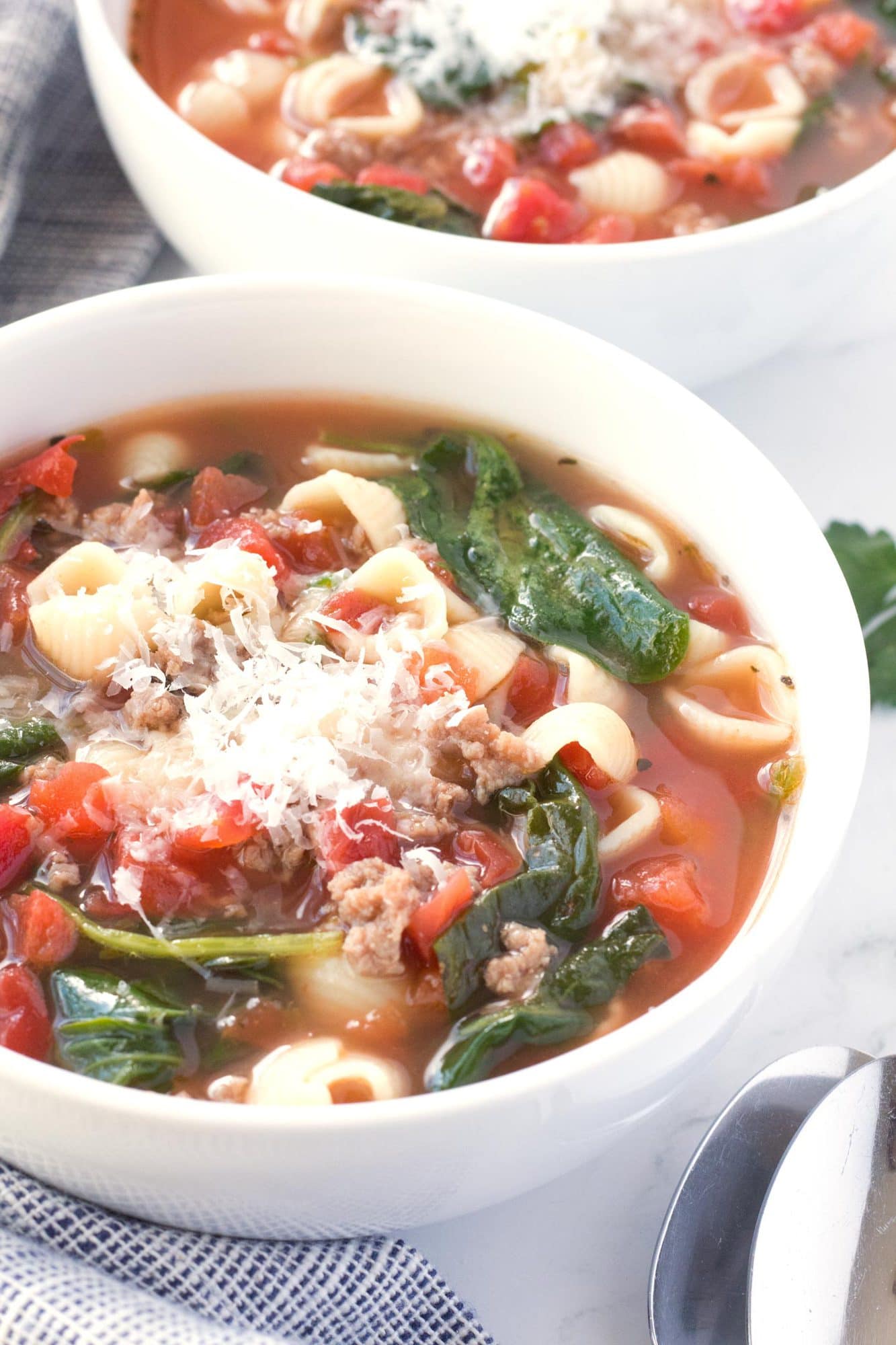 Bowl of sausage soup with spinach, tomatoes, parmesan, and pasta.
