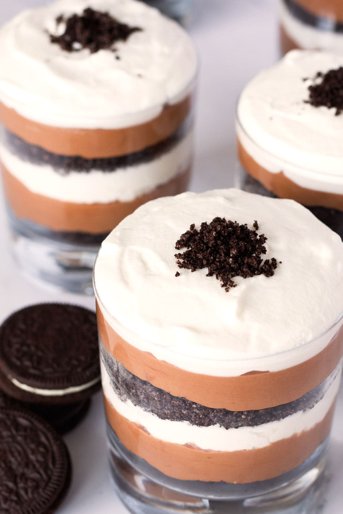 Chocolate parfaits with oreo crumbs on top and whole oreo cookies on counter.