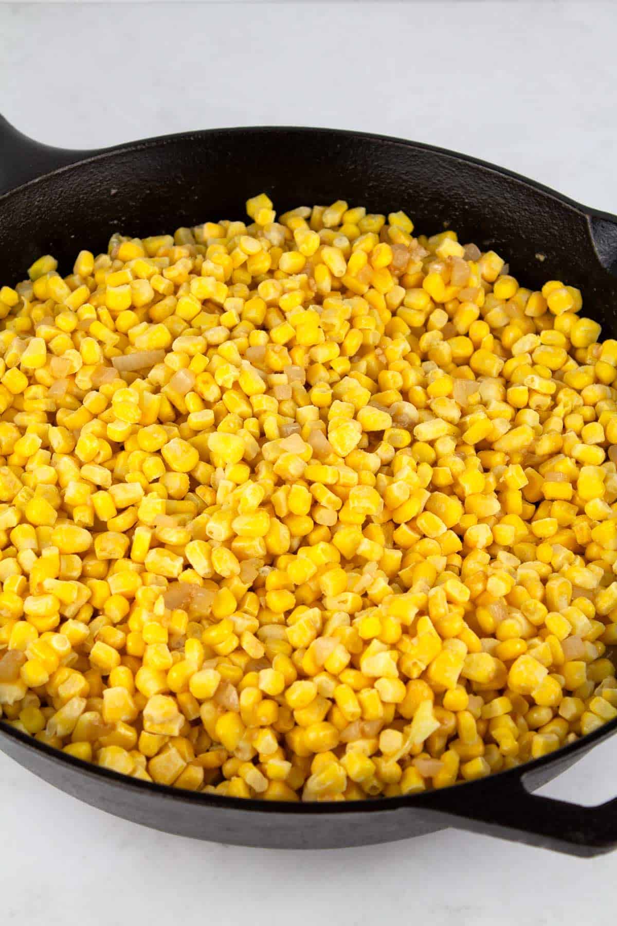 Frozen corn added to onions and garlic in skillet.
