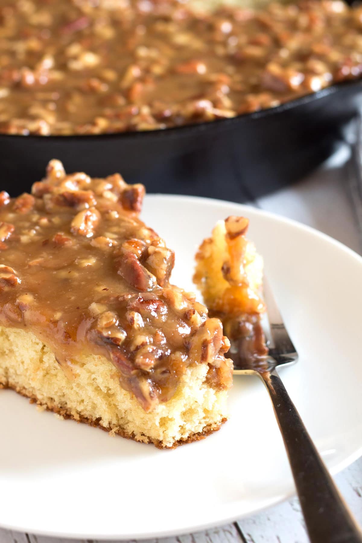 Skillet cake with caramel pecan topping dripping down the side and a bite on a fork.