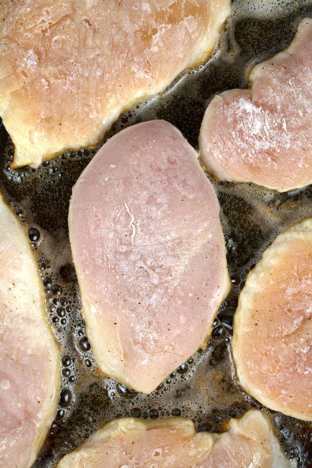 Overhead view of raw chicken cooking on the first side in a non-stick skillet.