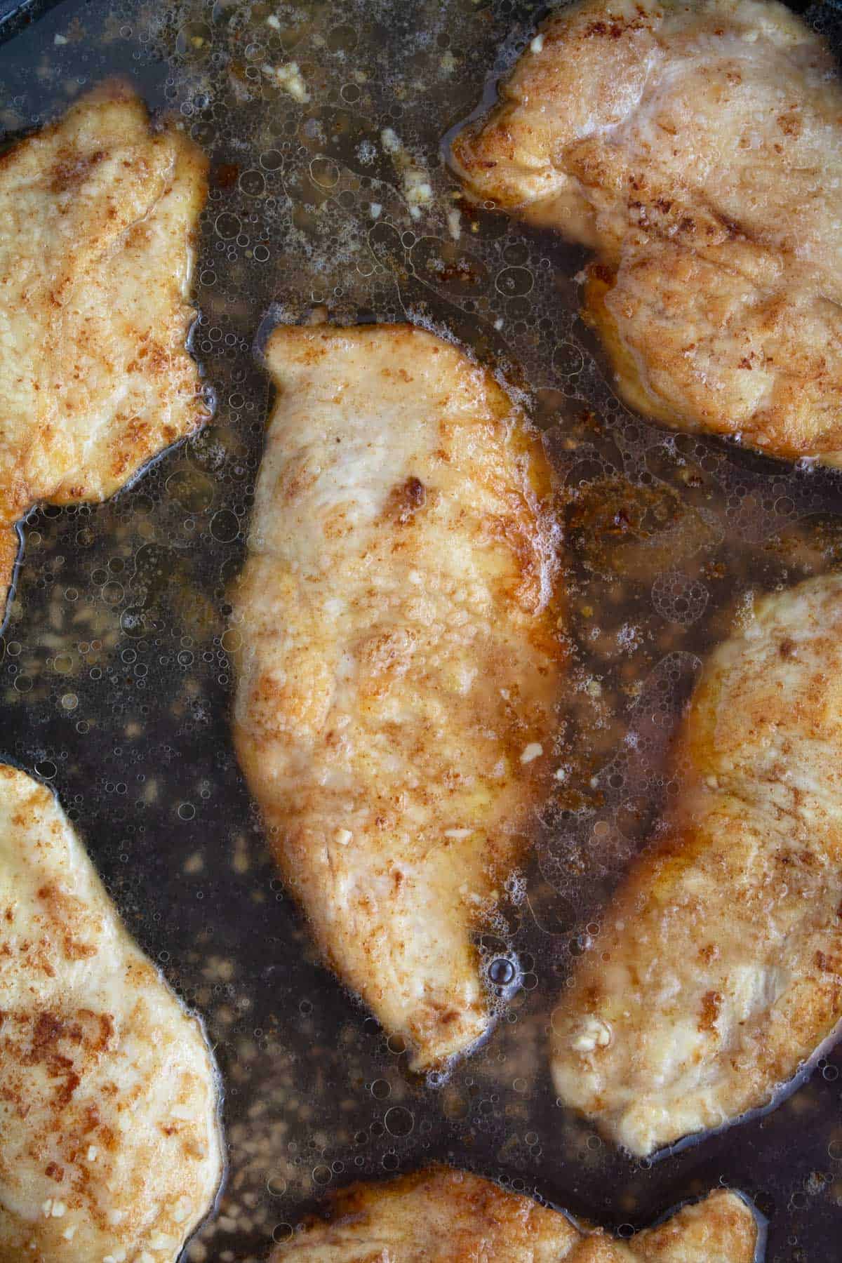 Overhead of chicken cooked in a non-stick skillet with white wine and chicken broth added to the pan.