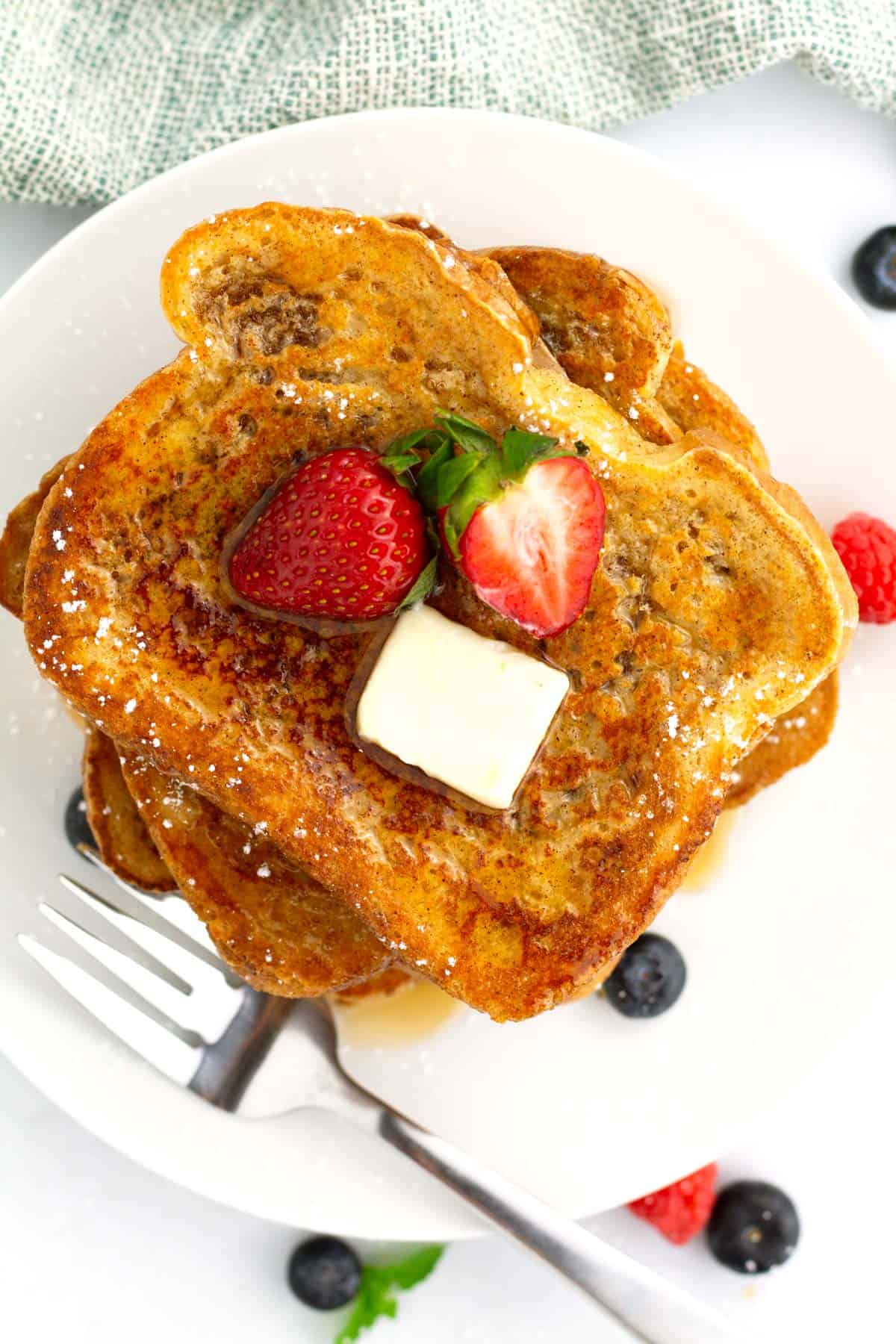 Pieces of simple french toast stacked together on a plate with fresh berries.