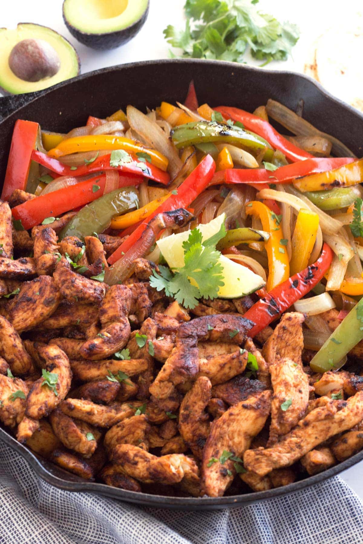 a 12-inch skillet filled with chicken fajitas, lime, avocado, and cilantro.