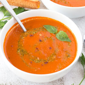 Spoon in a bowl of roasted tomato soup with grilled cheese in the background.