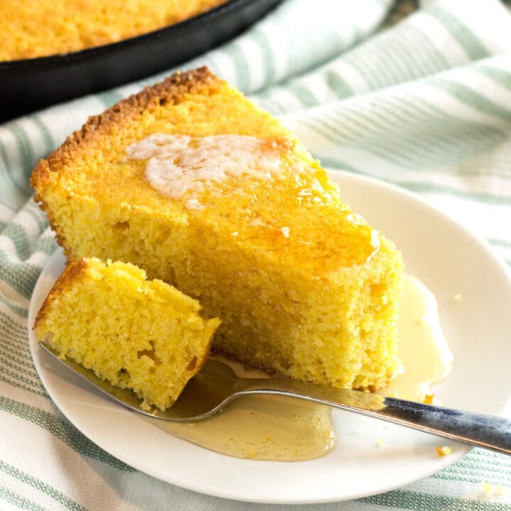 Fork with bite of cornbread resting on white plate.