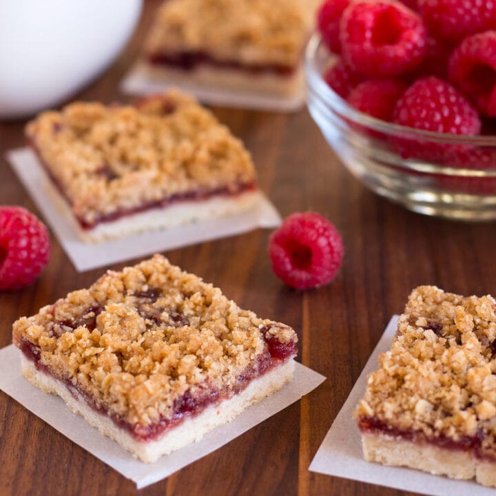 Raspberry bars with oatmeal crumble topping on cutting board with squares of parchment underneath.