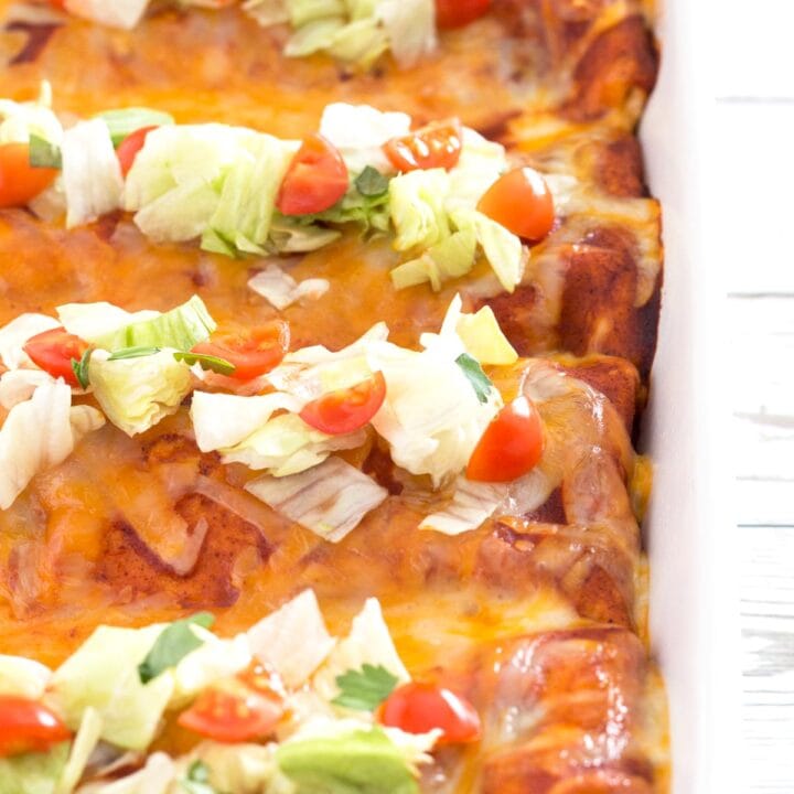 Baking dish with row of wet enchilada burritos with lettuce and tomato toppings.