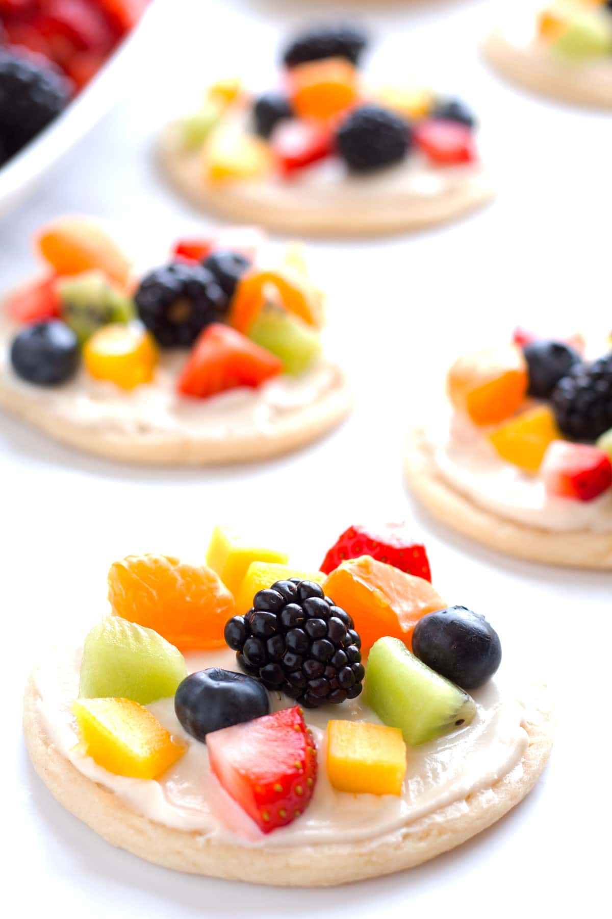 Single serve fruit pizza cookies on a counter topped with berries, kiwi, mango, and mandarins.