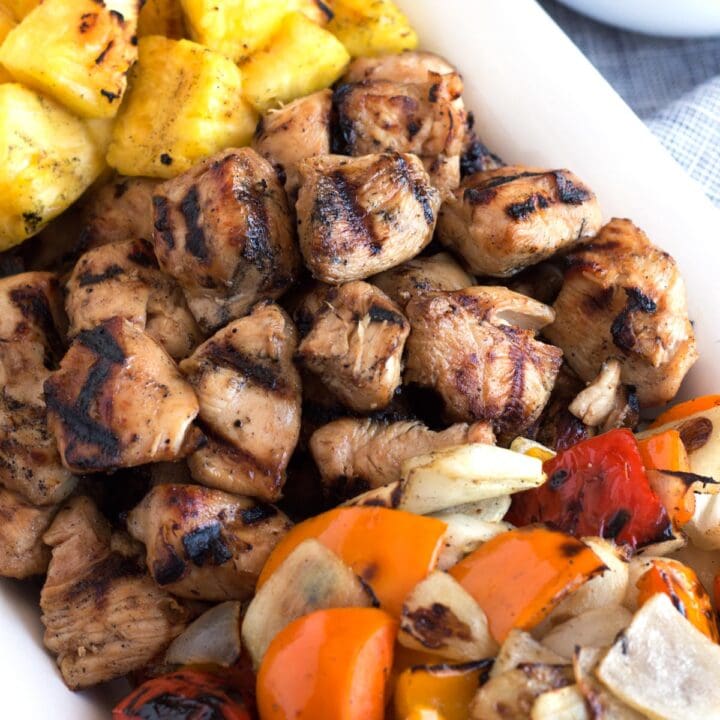 Close view of grilled chunks of marinated chicken next to grilled veggies and pineapple.