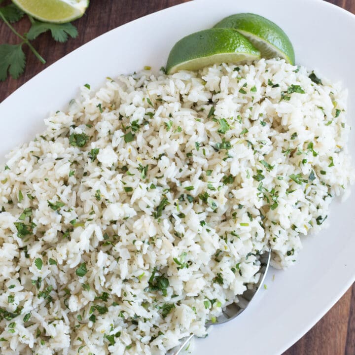 Oval platter of rice garnished with cilantro and lime wedges.