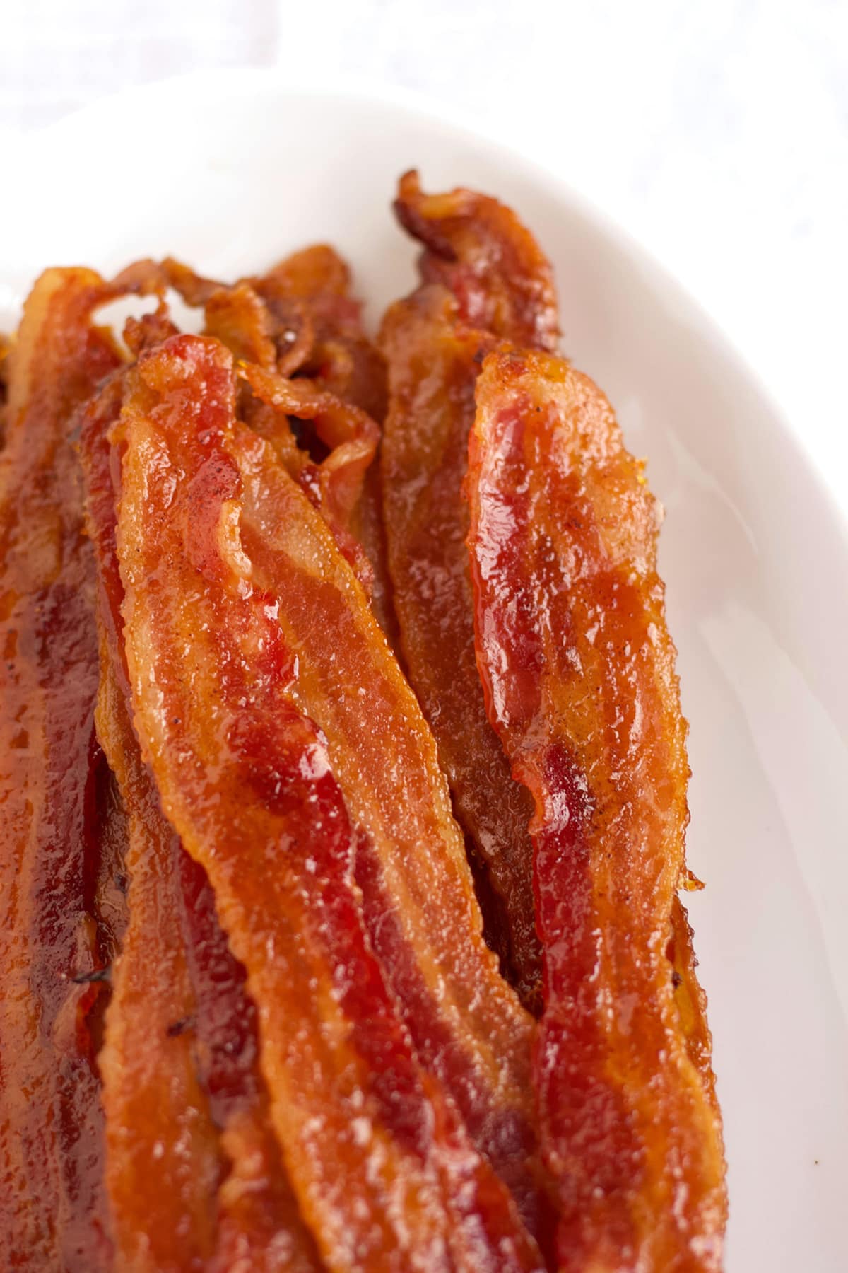 Slices of candied bacon on white platter for brunch. 