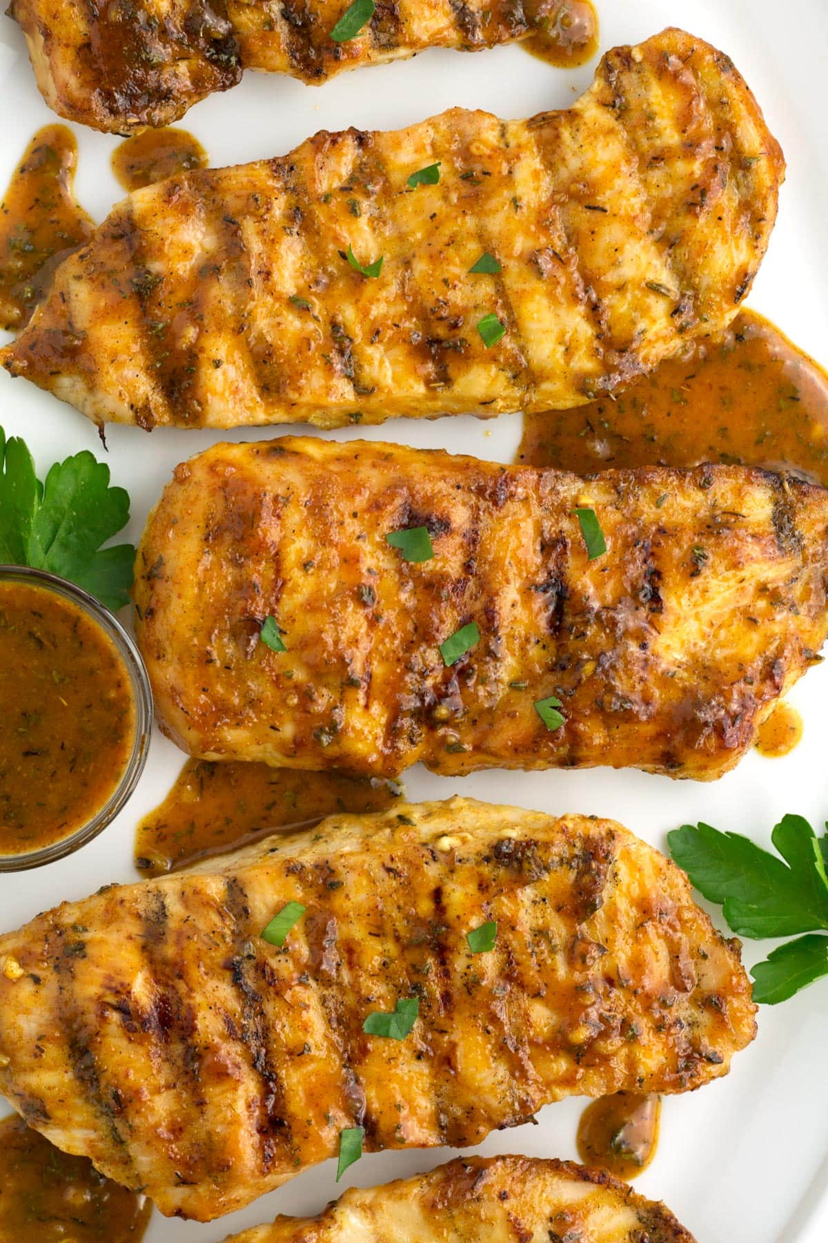 Overhead of three grilled chicken breasts with extra honey mustard sauce on the side.