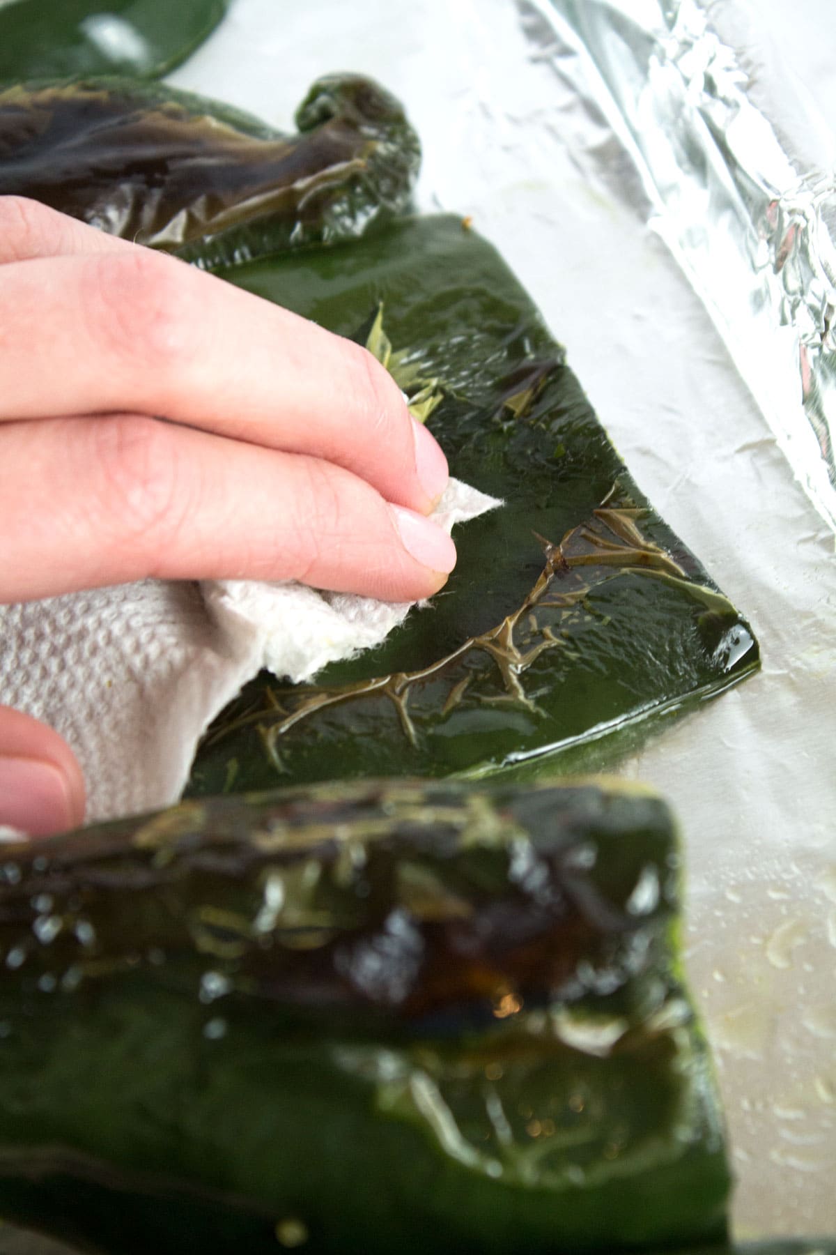 Hand removing charred portion of poblano skin with a paper towel.