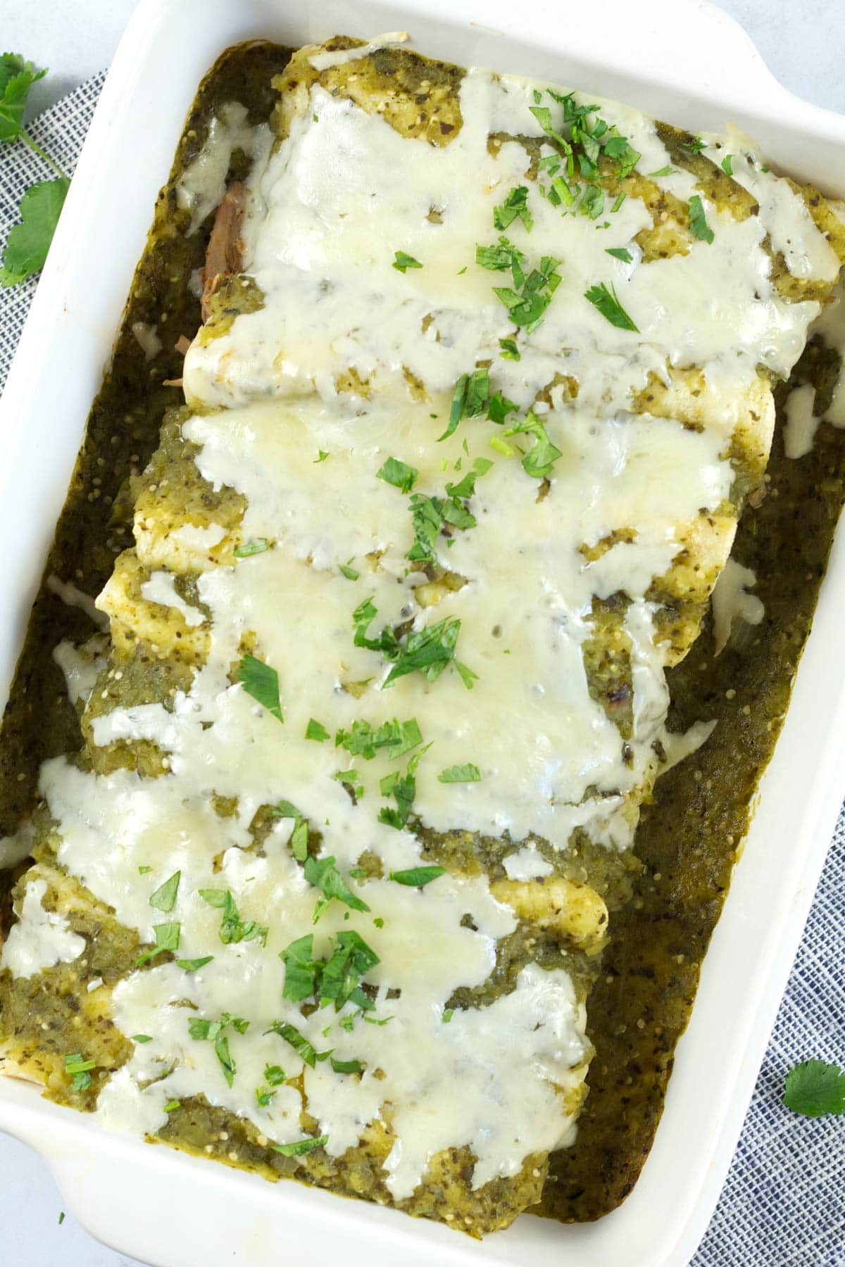 Pan of fully baked honey lime chicken enchiladas with green verde sauce.