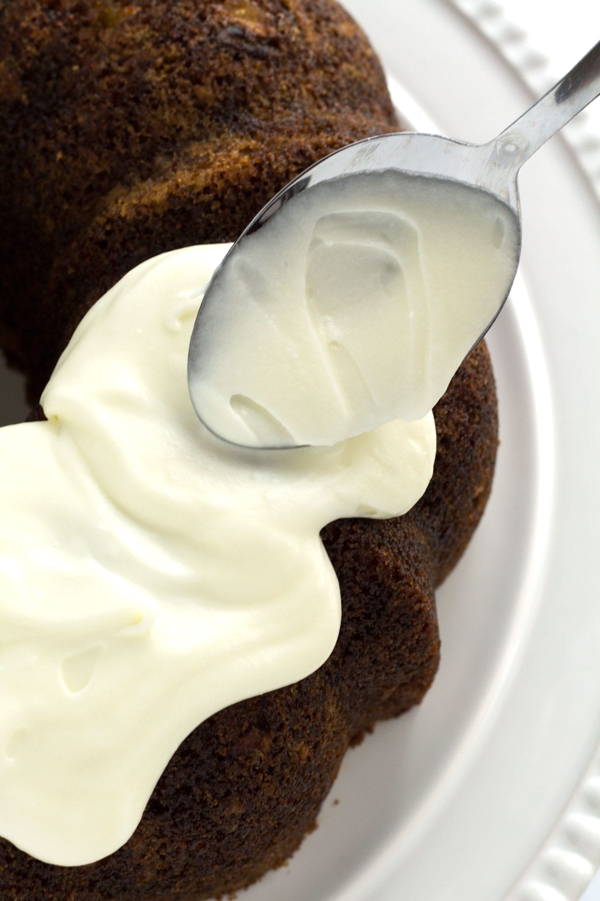 Decorating the top of a bundt cake with a spoon and cream cheese frosting.
