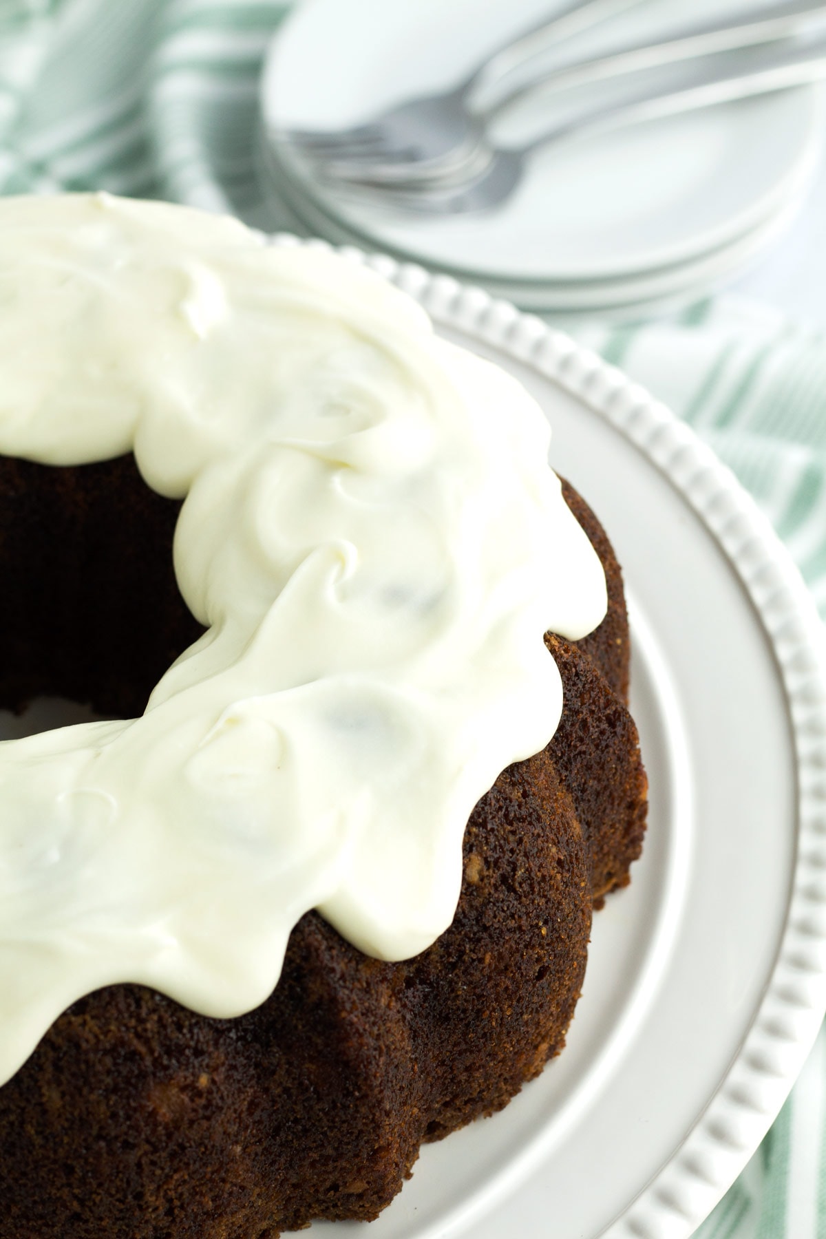 Whole bundt cake with cream cheese frosting on a cake plate.