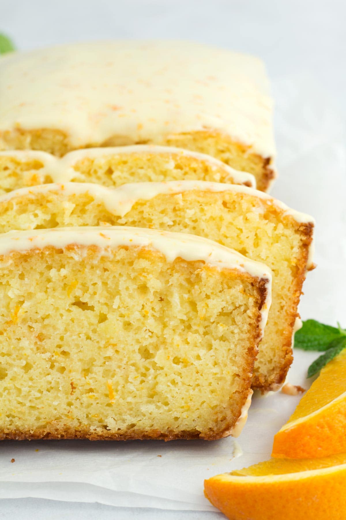 Staggered slices of orange loaf cake with glaze dripping off sides.