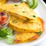 Three pieces of taco quesadillas made layered on a plate with fresh salsa and limes.