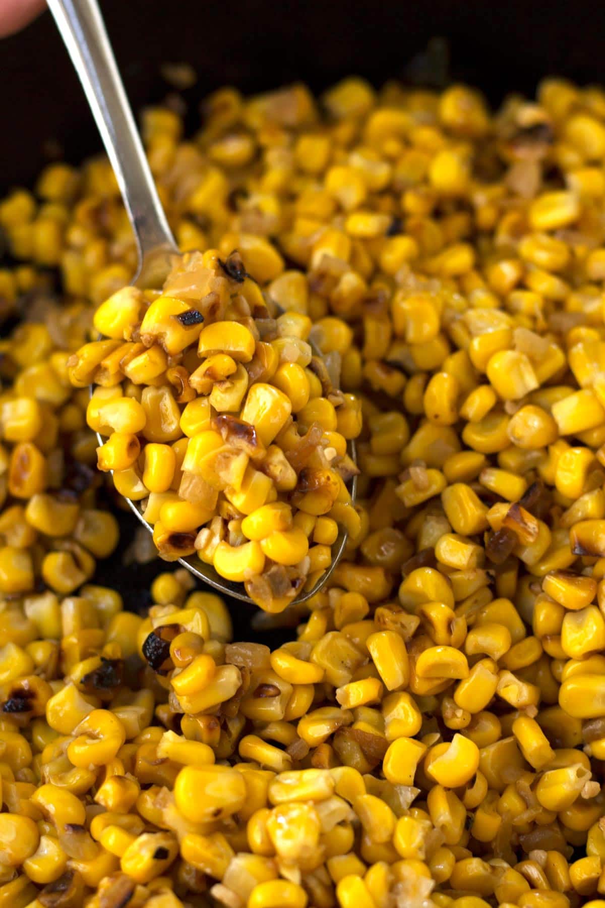 Spoon scooping caramelized roasted corn out of pan.