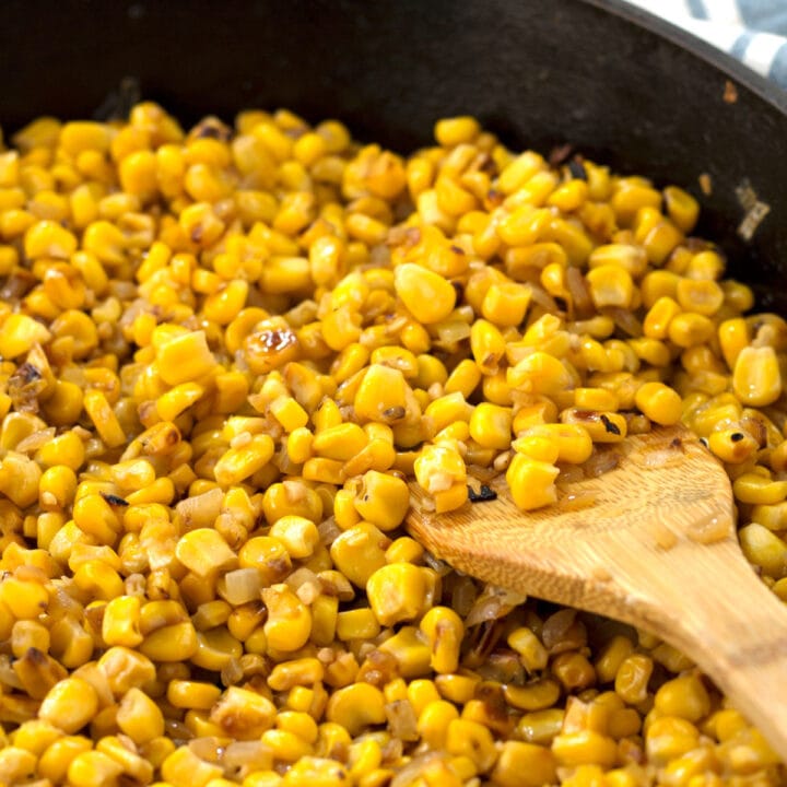 Whole corn kernels in cast iron skillet with a wooden spatula.
