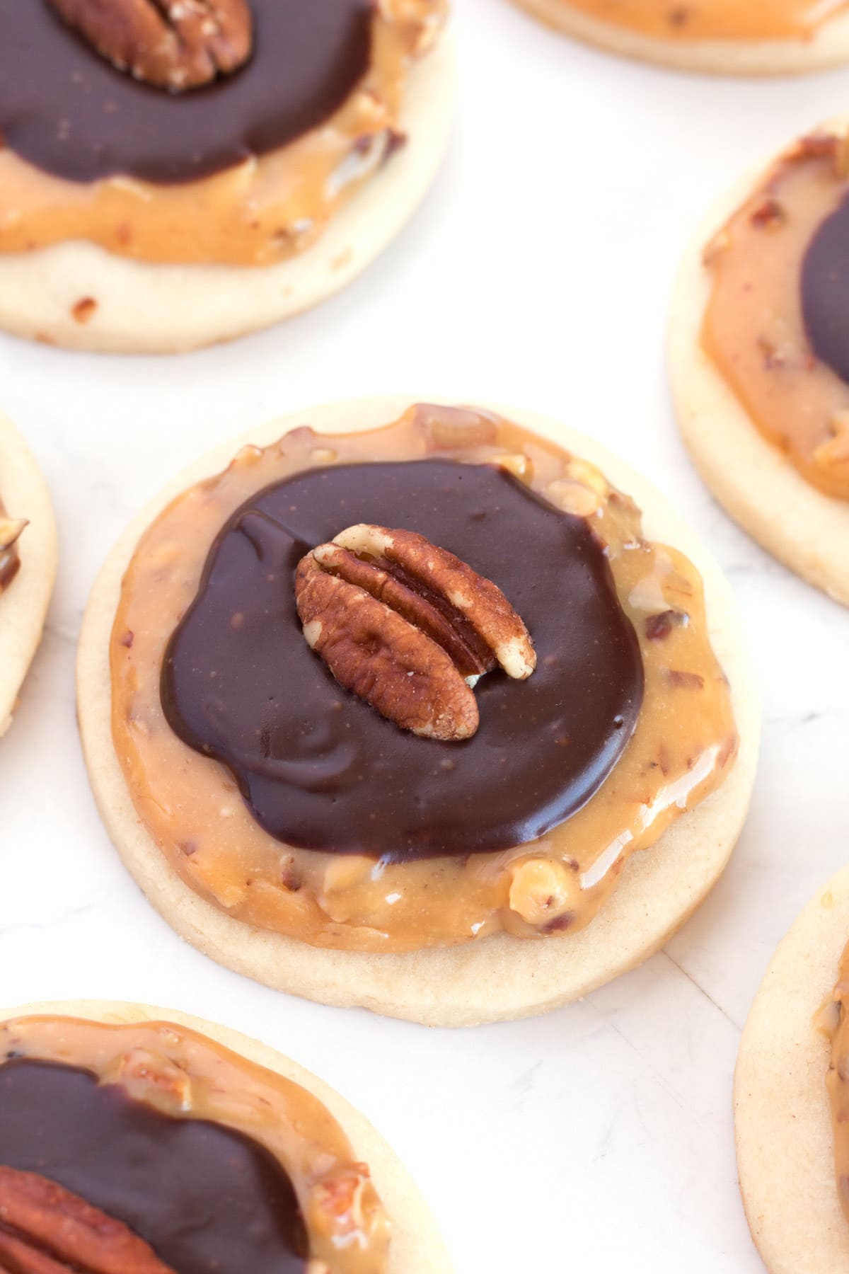 Close up of caramel shortbread cookies with chocolate and pecans on top.