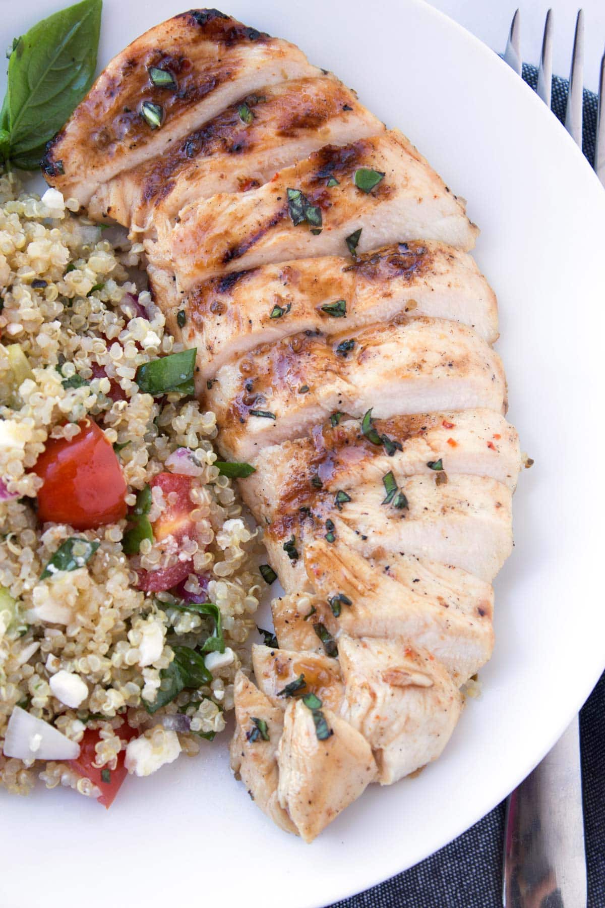 Grilled chicken sliced on a white plate with quinoa salad on the side.