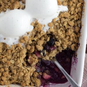 White baking dish with apple and blueberry crumble with ice cream scoops on top.