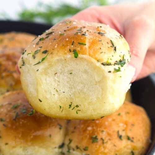 Baked Rhodes roll with butter and herbs being held in a hand.