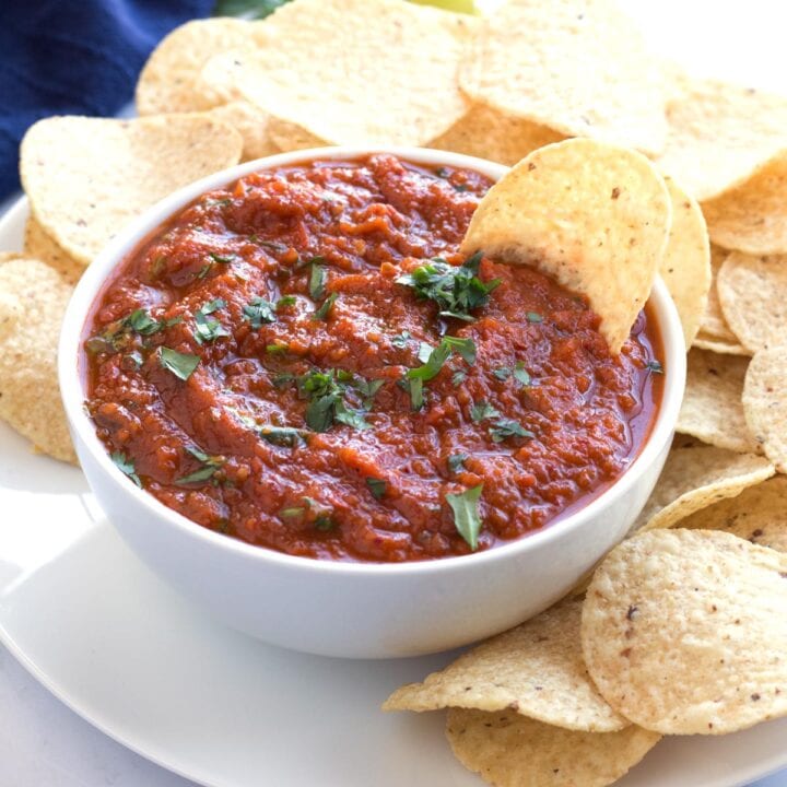 Bowl of Mexican salsa roja with chips on plate underneath.