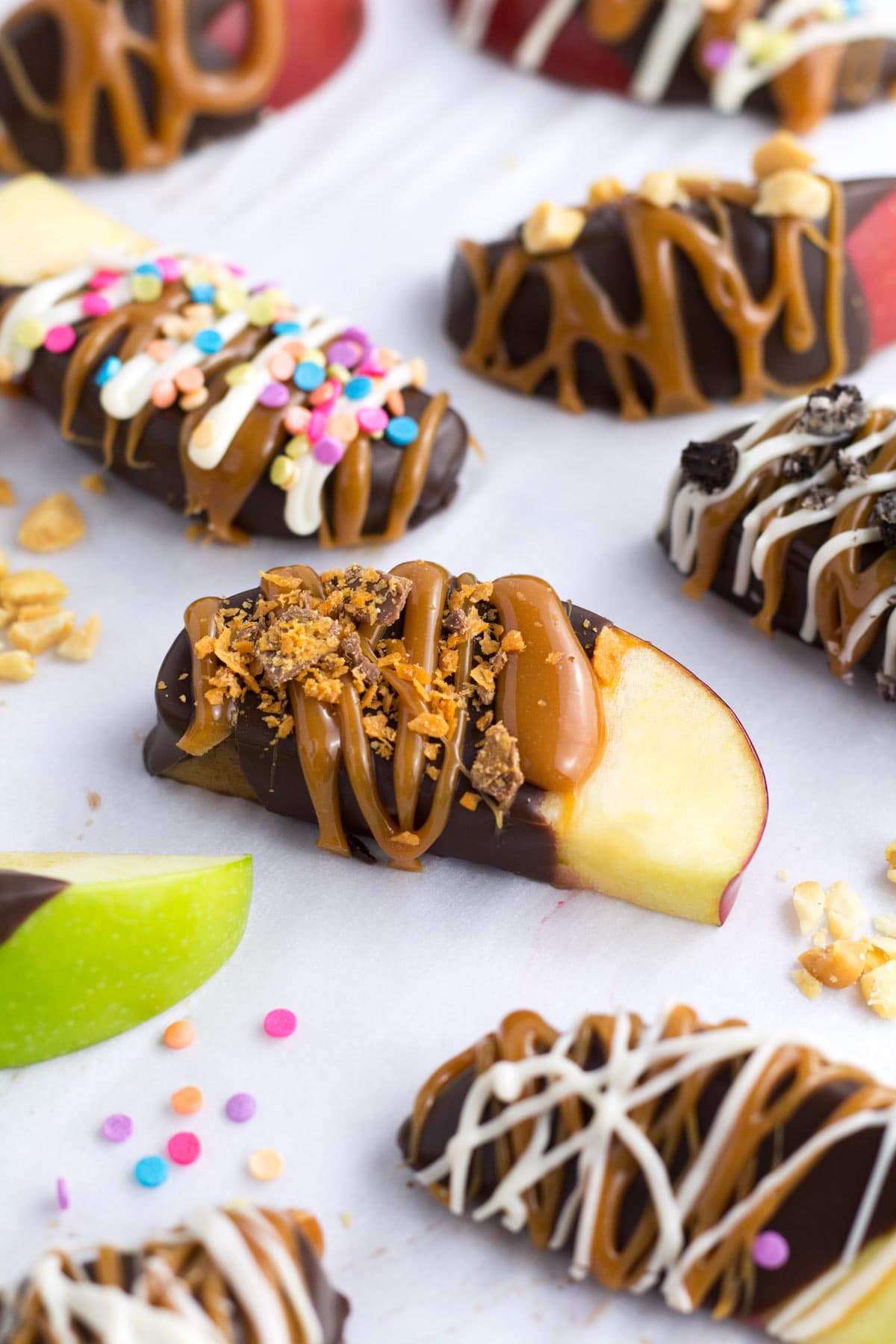 Caramel apple slices with different toppings on parchment paper.