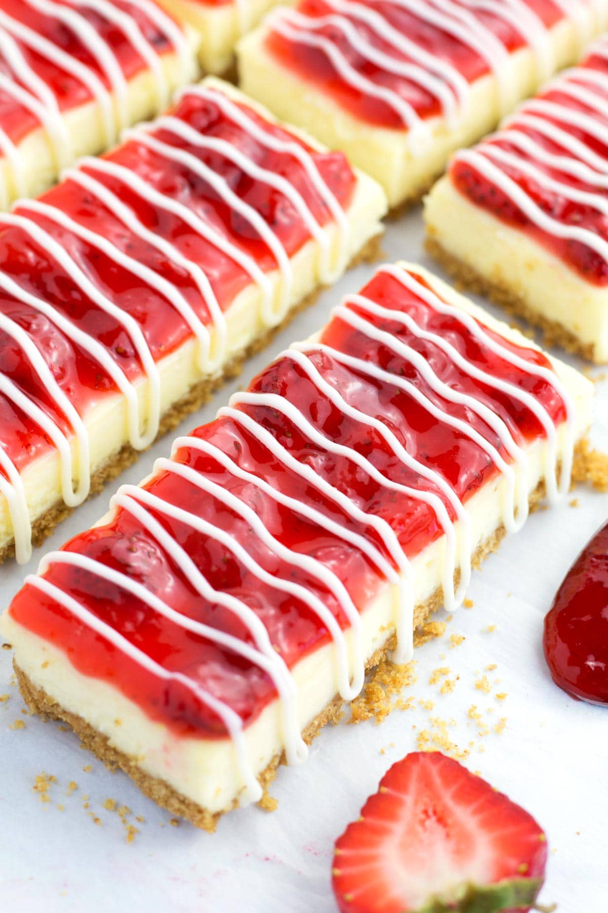 Rows of Philadelphia Cheesecake Bars with strawberry topping and white chocolate.