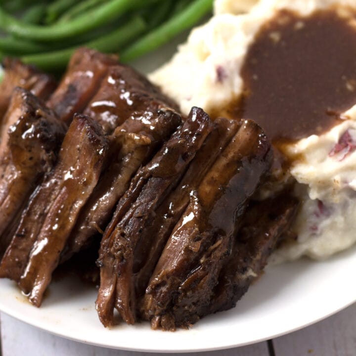 Tender roast beef on plate with mashed potatoes and green beans.