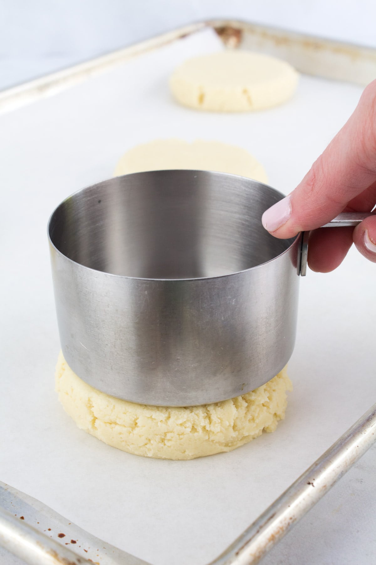Pressing scooped sugar cookies flat with a silver measuring cup.
